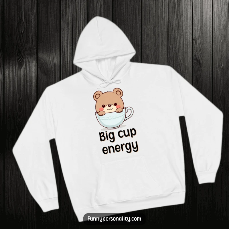 Funny hoodie featuring a smiling, curious bear character peering into an oversized teacup, offering cozy charm and a touch of humor.